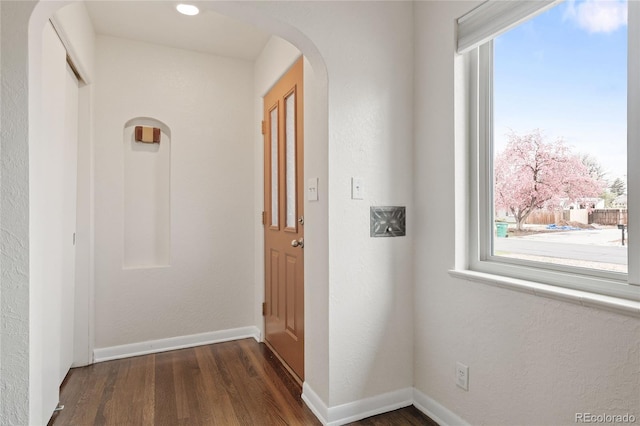 hall featuring arched walkways, baseboards, and dark wood-style floors
