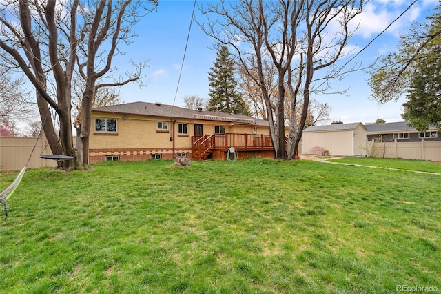 back of property with fence, a wooden deck, an outdoor structure, a lawn, and brick siding