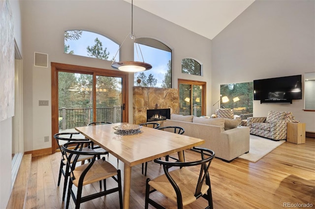 dining room with light wood-type flooring, baseboards, a fireplace, and high vaulted ceiling