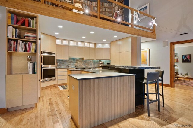 kitchen featuring a spacious island, tasteful backsplash, stainless steel double oven, modern cabinets, and light wood-type flooring