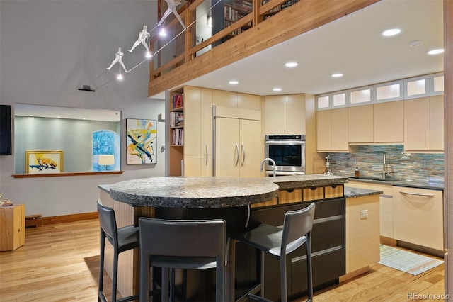 kitchen featuring a breakfast bar, paneled fridge, a sink, and an island with sink