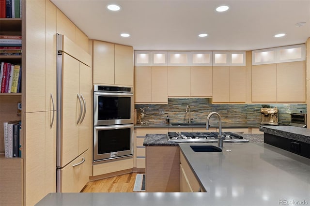 kitchen with stainless steel appliances, a sink, backsplash, and light wood finished floors