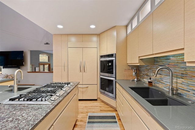 kitchen with light wood finished floors, tasteful backsplash, appliances with stainless steel finishes, and a sink