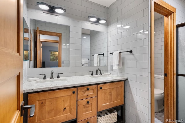 bathroom featuring a sink, tile walls, toilet, and double vanity