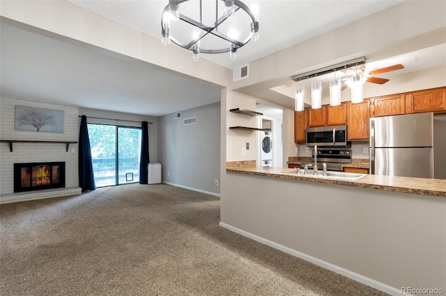 kitchen with sink, a brick fireplace, carpet, appliances with stainless steel finishes, and ceiling fan with notable chandelier