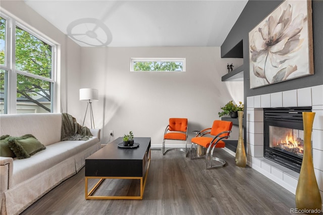 living area with wood finished floors, plenty of natural light, a tile fireplace, and baseboards