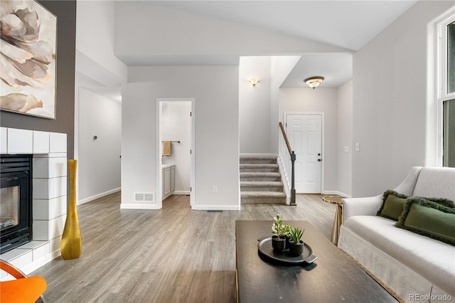 living room with light wood-type flooring, stairway, baseboards, lofted ceiling, and a tiled fireplace