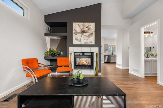 living room featuring wood finished floors, a tile fireplace, lofted ceiling, and baseboards