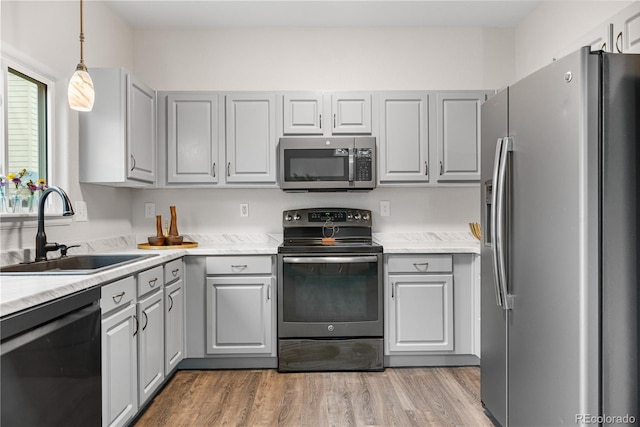 kitchen featuring stainless steel appliances, a sink, gray cabinetry, light wood finished floors, and pendant lighting