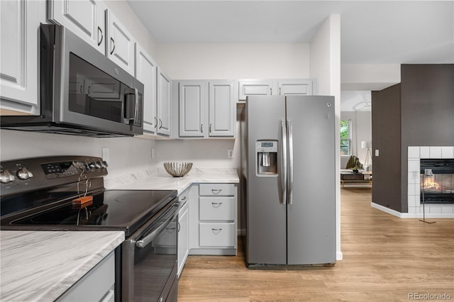 kitchen with stainless steel appliances, light wood-type flooring, light stone countertops, and baseboards