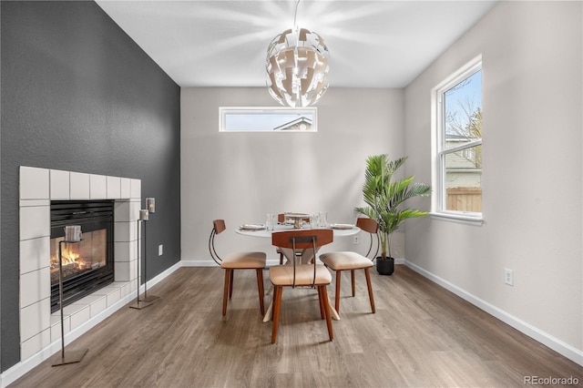 dining area featuring a chandelier, wood finished floors, baseboards, and a tiled fireplace