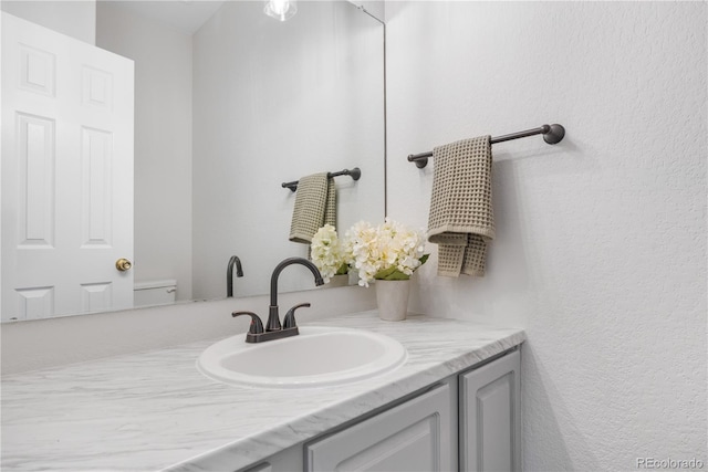 bathroom featuring vanity, a textured wall, and toilet