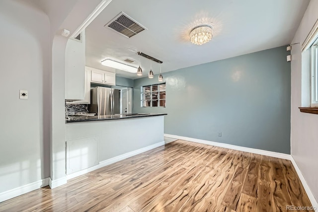 kitchen with hanging light fixtures, light wood-type flooring, tasteful backsplash, white cabinetry, and stainless steel refrigerator