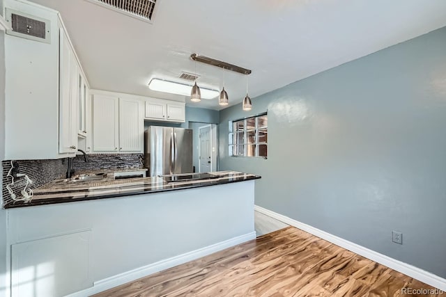 kitchen with stainless steel fridge, backsplash, sink, white cabinets, and hanging light fixtures