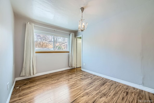 spare room with a chandelier and wood-type flooring