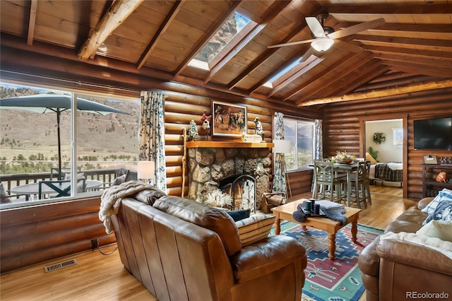 9850 Mohawk Trl, Cascade, CO 80809 - living area featuring wood finished floors, a ceiling fan, a skylight, a stone fireplace, and log walls