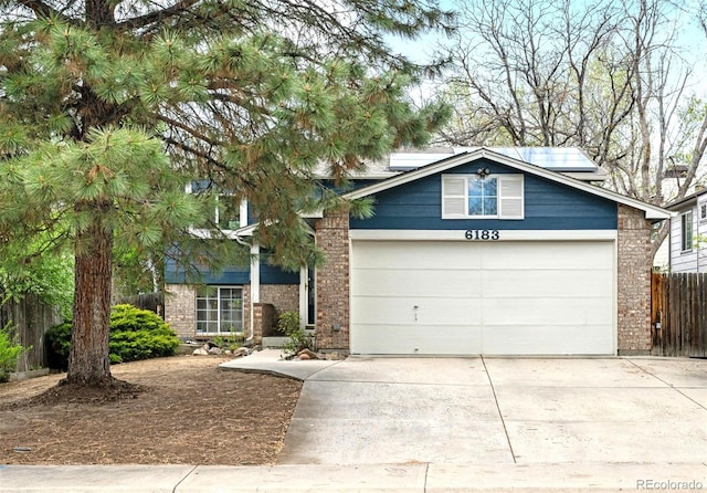 view of front of home with fence, an attached garage, brick siding, solar panels, and driveway