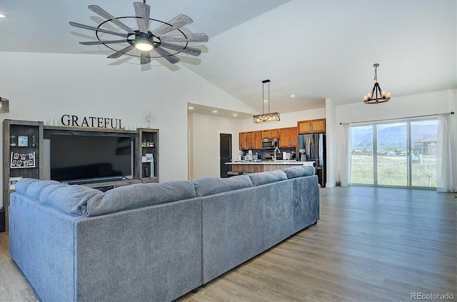 living room featuring ceiling fan with notable chandelier, high vaulted ceiling, sink, and light hardwood / wood-style floors