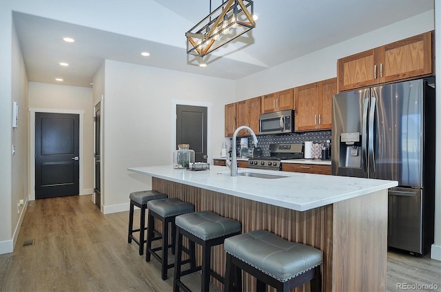 kitchen featuring a breakfast bar, backsplash, hanging light fixtures, a kitchen island with sink, and stainless steel appliances