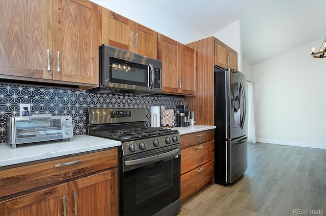 kitchen featuring lofted ceiling, decorative backsplash, stainless steel appliances, and light wood-type flooring