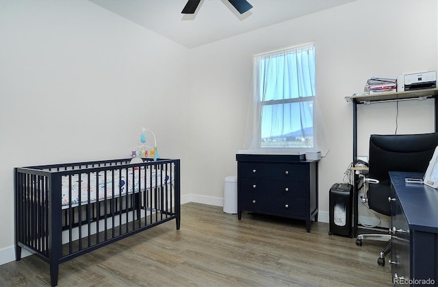 bedroom with a crib, hardwood / wood-style floors, and ceiling fan