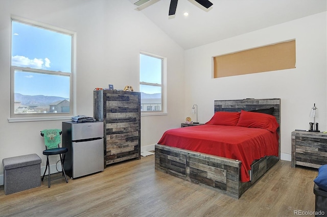 bedroom with stainless steel fridge, ceiling fan, light hardwood / wood-style floors, a mountain view, and vaulted ceiling