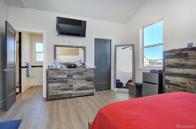 bedroom featuring lofted ceiling, light hardwood / wood-style floors, and stainless steel refrigerator