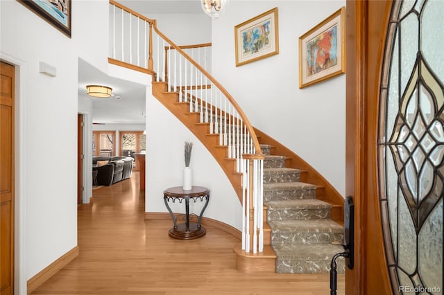 stairs featuring wood finished floors, a high ceiling, and baseboards