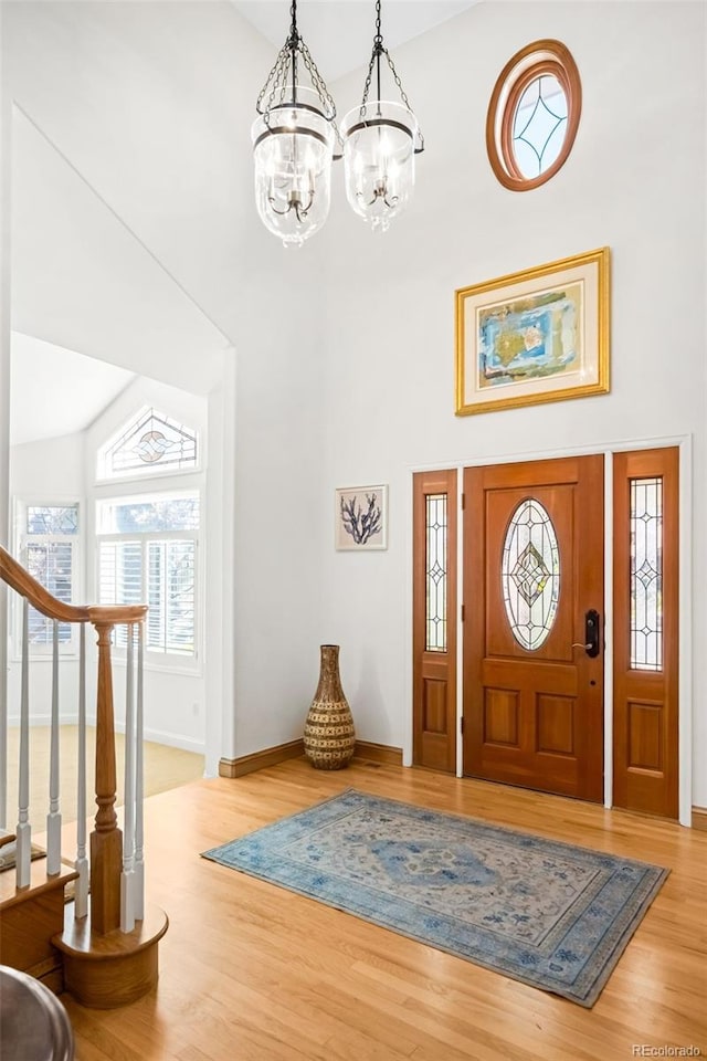foyer with wood finished floors, a towering ceiling, baseboards, and a notable chandelier