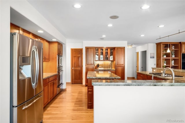 kitchen featuring recessed lighting, brown cabinetry, decorative backsplash, light wood-style flooring, and appliances with stainless steel finishes
