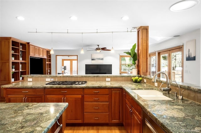 kitchen with a sink, stone counters, stainless steel gas stovetop, a ceiling fan, and open shelves