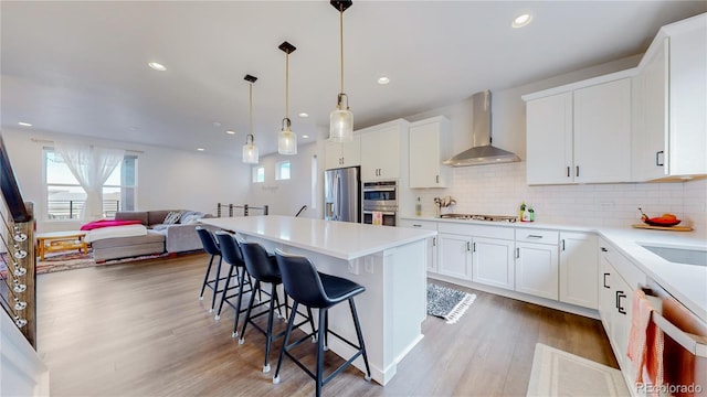 kitchen featuring stainless steel appliances, a kitchen island, white cabinets, wall chimney range hood, and a kitchen bar