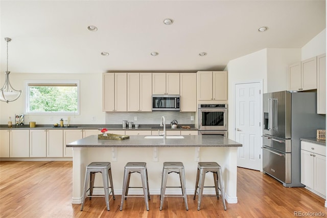 1477 Serene Dr, Erie, CO 80516 - kitchen with appliances with stainless steel finishes, a sink, a breakfast bar area, decorative backsplash, and an island with sink