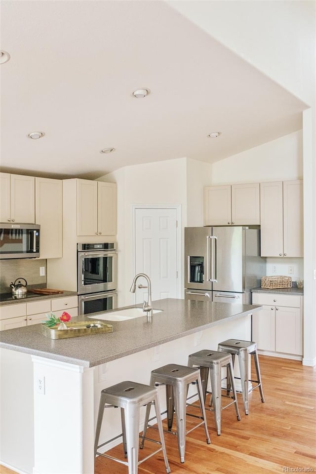 1477 Serene Dr, Erie, CO 80516 - kitchen featuring stainless steel appliances, a kitchen breakfast bar, light wood-type flooring, light stone countertops, and a kitchen island with sink