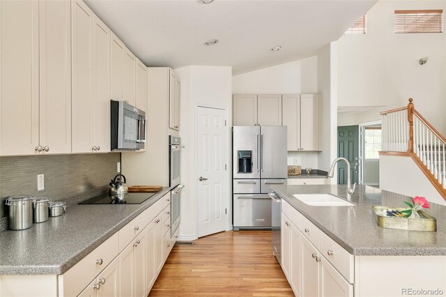 1477 Serene Dr, Erie, CO 80516 - kitchen featuring appliances with stainless steel finishes, a sink, a center island with sink, light wood finished floors, and backsplash