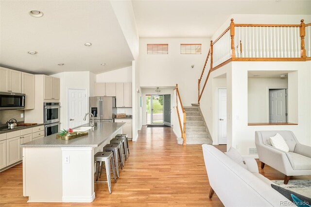 1477 Serene Dr, Erie, CO 80516 - kitchen with appliances with stainless steel finishes, a sink, a breakfast bar area, light wood finished floors, and a towering ceiling