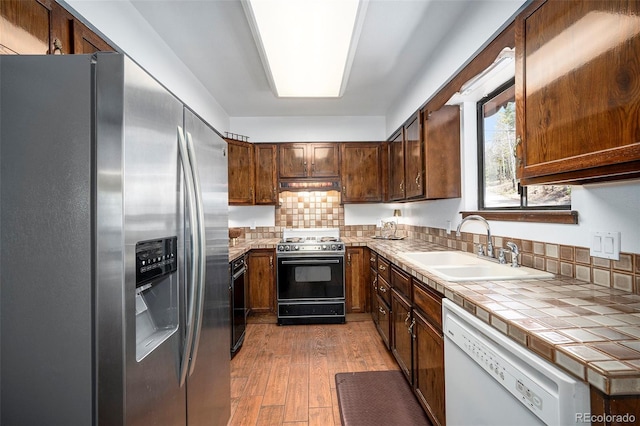 kitchen with stainless steel refrigerator with ice dispenser, light wood-type flooring, dishwasher, a sink, and gas range oven