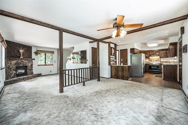 unfurnished living room with dark carpet, a ceiling fan, a sink, and a stone fireplace
