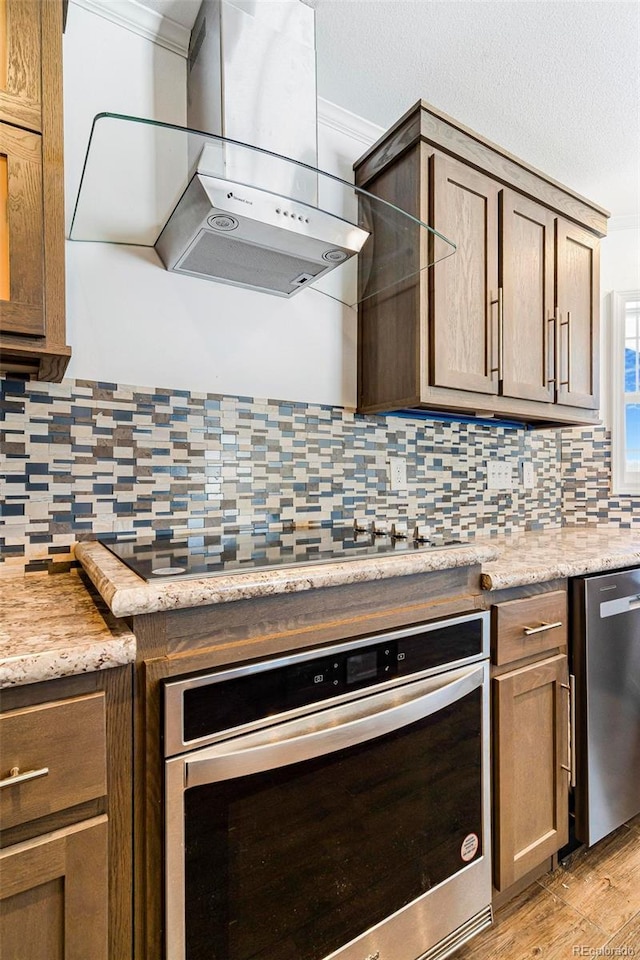 kitchen with ornamental molding, appliances with stainless steel finishes, backsplash, and range hood