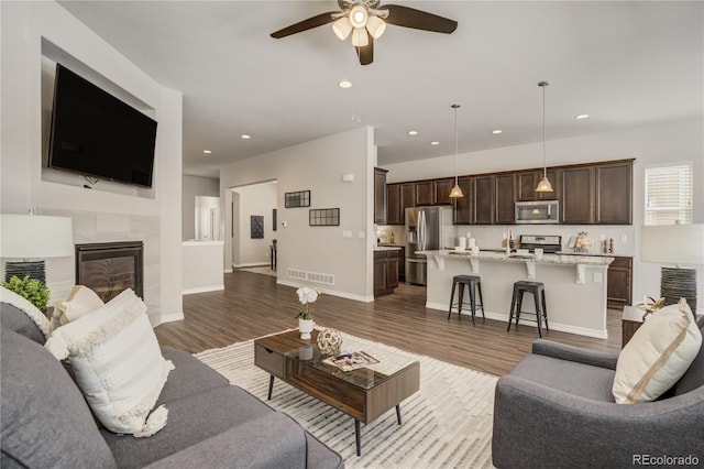 living area with recessed lighting, visible vents, a tiled fireplace, and wood finished floors