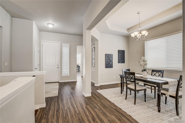 dining area featuring dark wood-type flooring, a tray ceiling, a notable chandelier, and baseboards