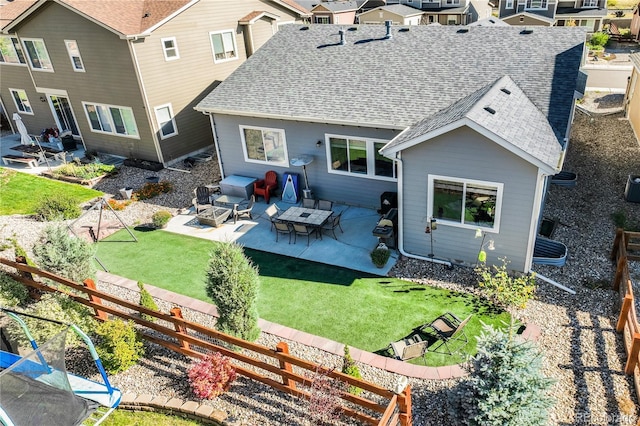 back of property with a fire pit, a yard, a shingled roof, and a patio area