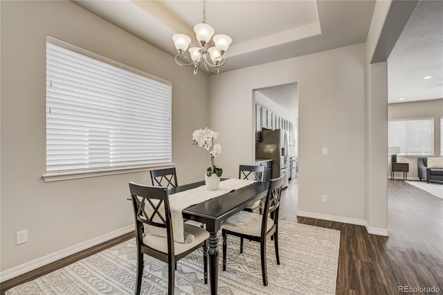 dining space with a raised ceiling, a notable chandelier, baseboards, and wood finished floors