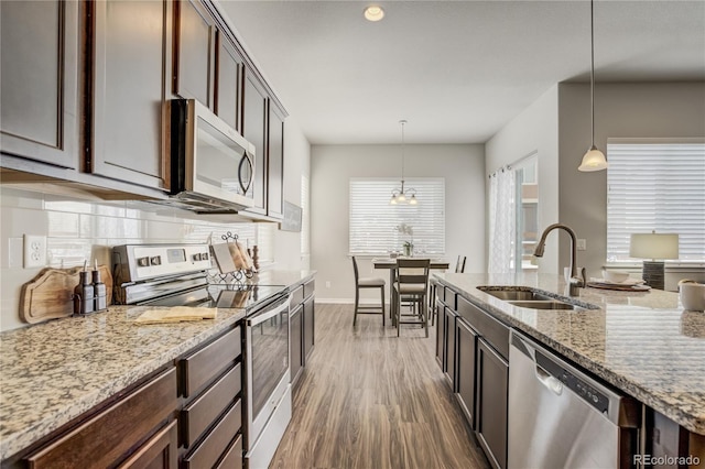 kitchen featuring light stone counters, wood finished floors, a sink, appliances with stainless steel finishes, and backsplash