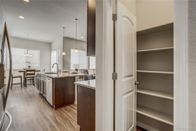 kitchen featuring light stone counters, stainless steel appliances, wood finished floors, dark brown cabinets, and an island with sink