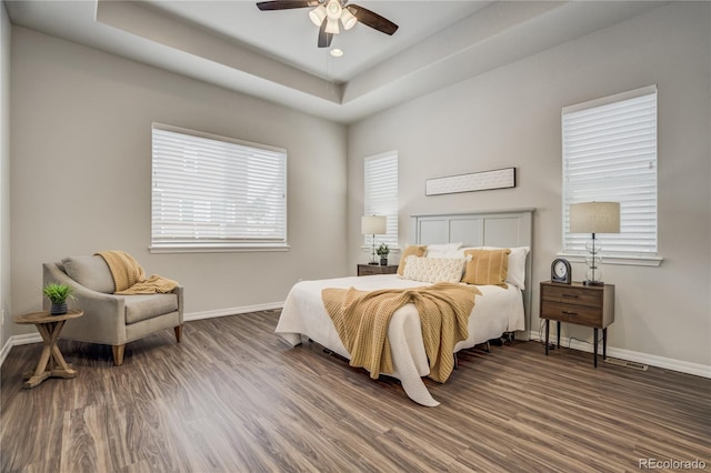 bedroom featuring a raised ceiling, baseboards, and wood finished floors