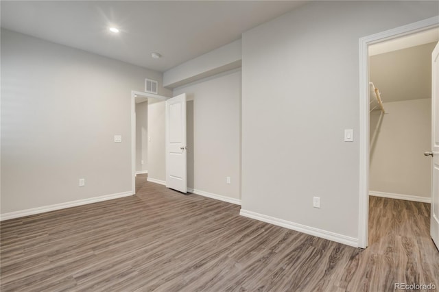 unfurnished bedroom featuring baseboards, visible vents, a walk in closet, and wood finished floors