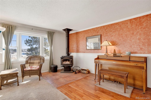 living area with ornamental molding, light hardwood / wood-style floors, a textured ceiling, and a wood stove