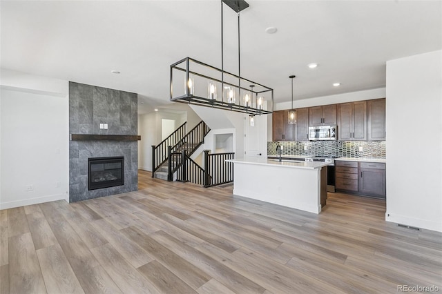 28564 E 6th Pl, Watkins, CO 80137 - kitchen featuring appliances with stainless steel finishes, open floor plan, light wood-style flooring, light countertops, and a tile fireplace