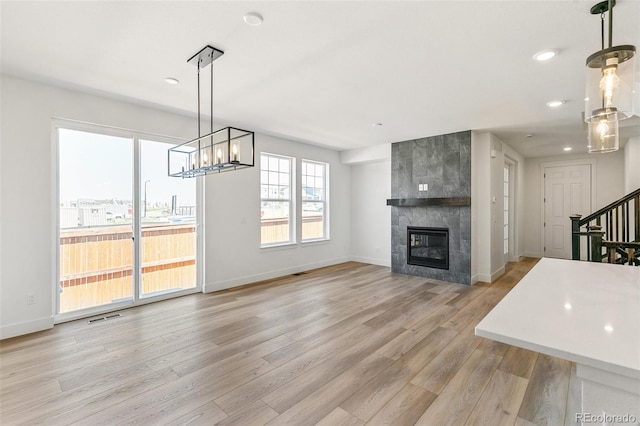 28564 E 6th Pl, Watkins, CO 80137 - unfurnished living room featuring light wood-type flooring, a chandelier, a tiled fireplace, stairway, and recessed lighting